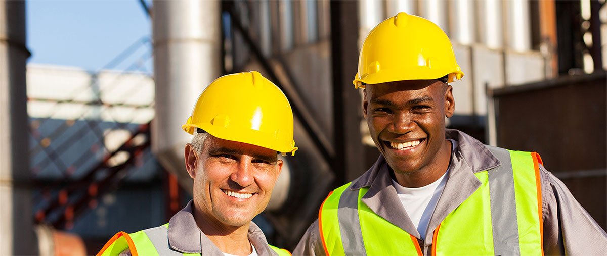 Two smiling men in safety gear outside a plant